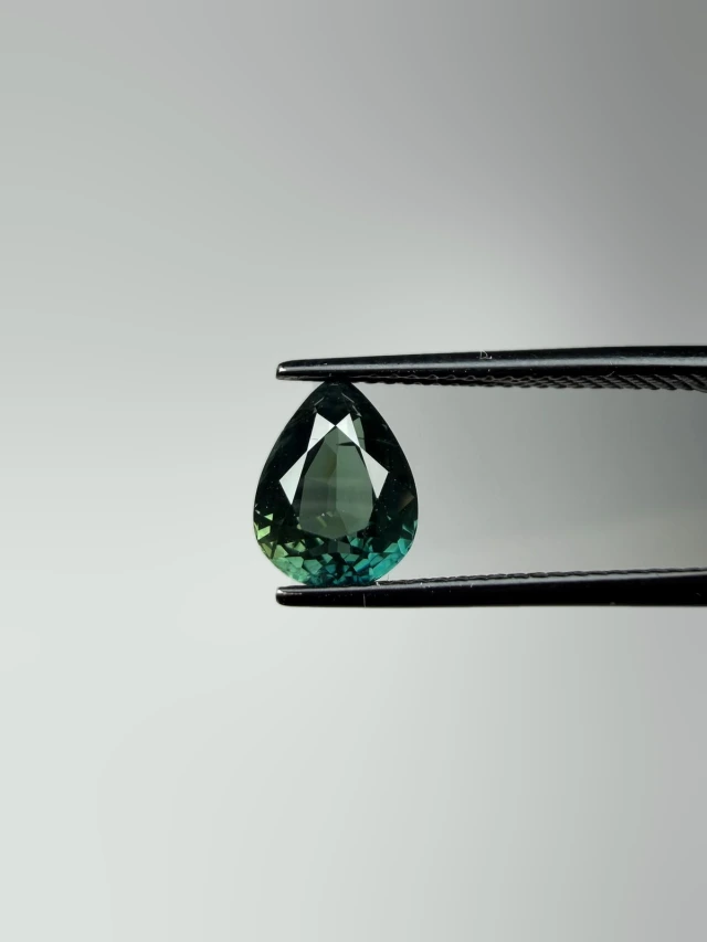 Teal pear-cut sapphire held in tweezers